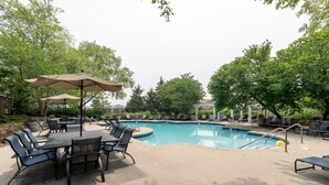 A poolside area with a pool, lounge chairs, and a table with chairs. - Affordable 1-bedroom Apartment Keystone (Indianapolis)