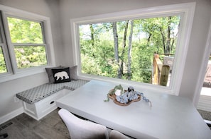 Quarto com uma janela grande, um banquinho com almofada de urso e uma coruja decorativa sobre um tabuleiro.