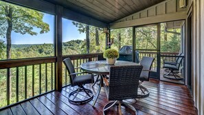 Une terrasse extérieure couverte, dotée d’une table ronde et de chaises en osier, qui offre une vue sur une zone boisée.