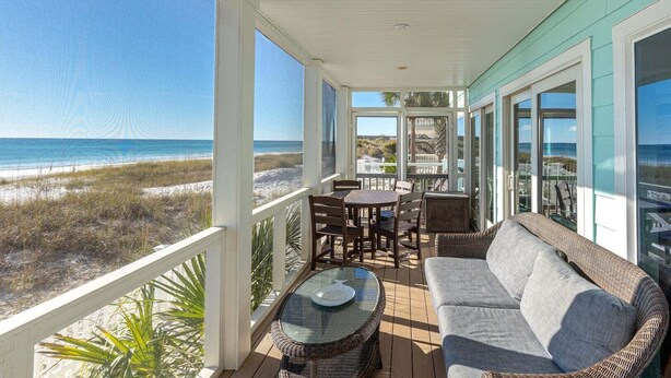 A covered outdoor area with a view of the beach, a table, chairs, and a sofa. - Diamond Dunes (Panama City Beach)