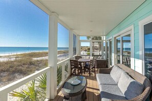 Ein überdachter Außenbereich mit Blick auf den Strand, inklusive Tisch, Stühle und einer Couch.