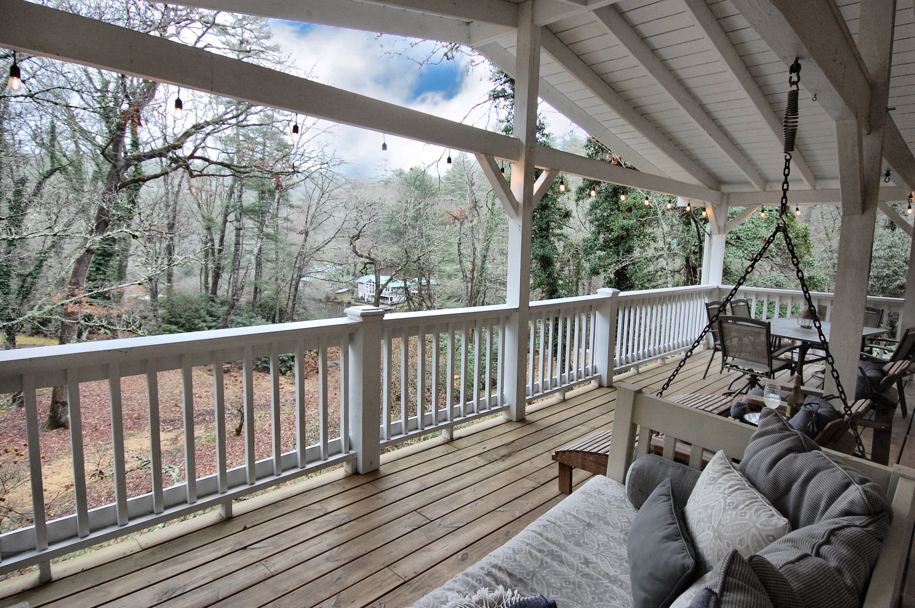A wooden deck with a white railing, a hanging chair, and a sofa with cushions.