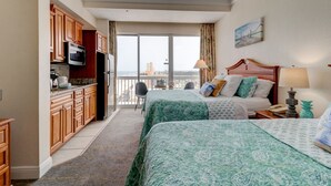 Ein Hotelzimmer mit zwei Betten, einer Küchenzeile und einem Balkon mit Blick auf die Stadt.