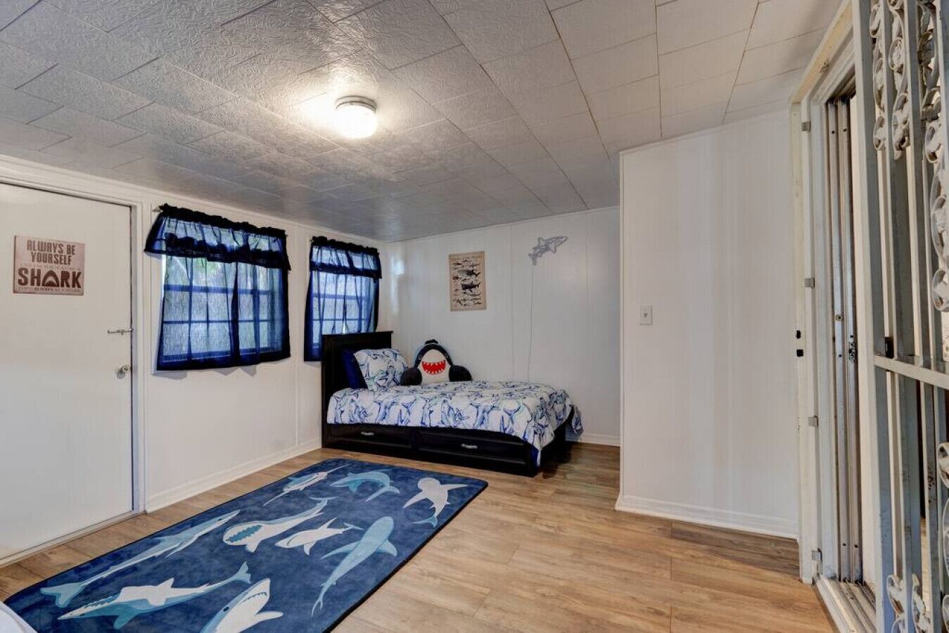 Een slaapkamer met een bed, een raam met gordijnen, een deur met een bordje en een houten vloer.