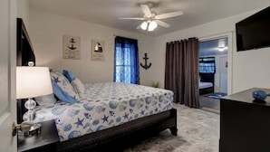 Un dormitorio con cama, ventilador de techo, mesita de noche, lámpara y televisor.