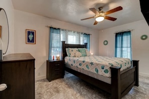 A bedroom with a bed, a nightstand, a dresser, a ceiling fan, and a window with curtains. - Shark Shack Large House Minutes to the Beach (Holly Hill)