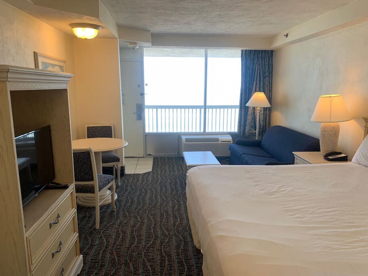 Een hotelkamer met een bed, een bureau, een televisie, een stoel, een bank en een balkon met uitzicht.