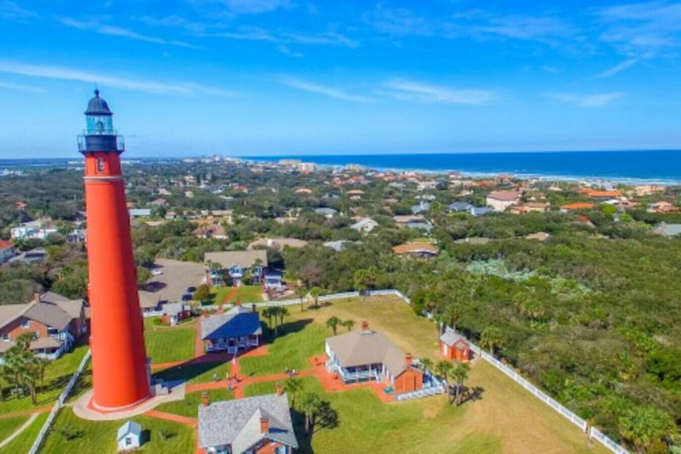 A red lighthouse with a clear view of the surrounding residential area and ocean.
