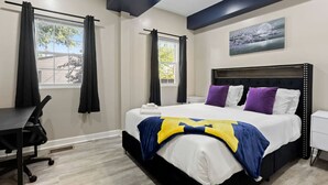A modern hotel room with a large bed, a desk, and a window with curtains. - Modern Comfort Downtown Indy Stylish 3BR Getaway (Indianapolis)