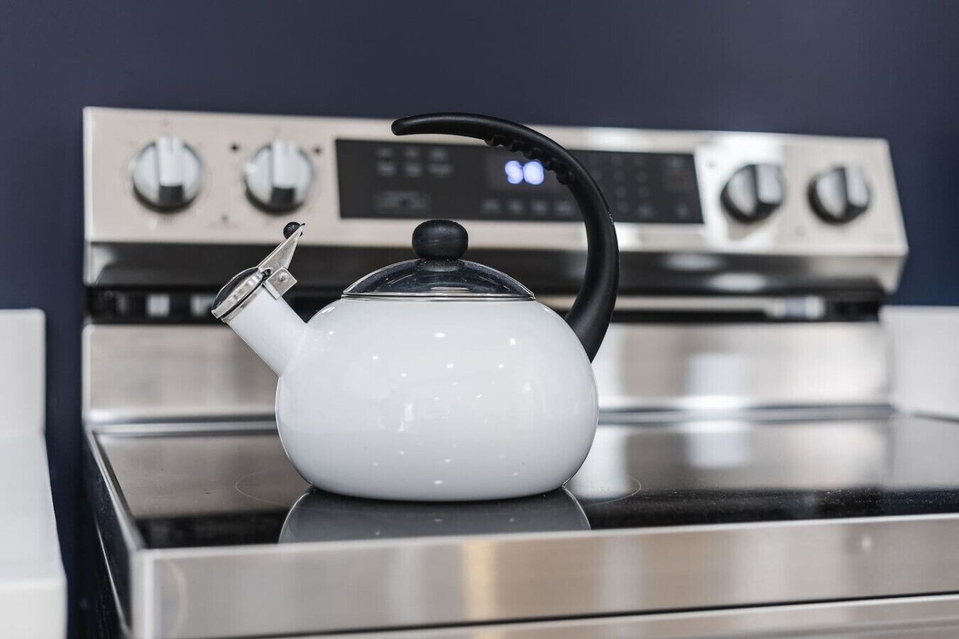 A white kettle on a stove with a digital control panel in the background.