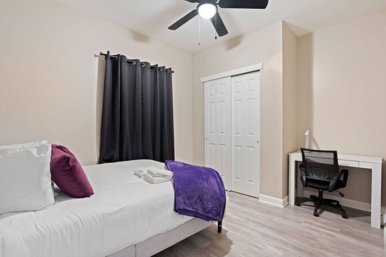 Un dormitorio con cama, escritorio, silla, ventilador de techo y armario.