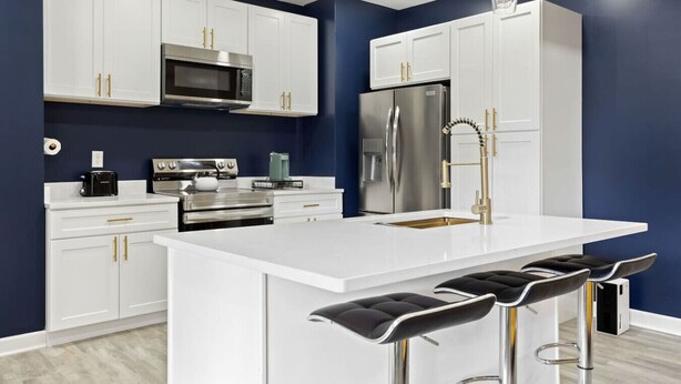 A modern kitchen with white cabinetry, stainless steel appliances, and a central island with bar stools. - Modern Comfort Downtown Indy Stylish 3BR Getaway (Indianapolis)