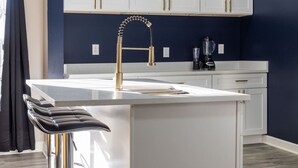 A modern kitchen with a central island, white cabinetry, and a gold faucet. - Modern Comfort Downtown Indy Stylish 3BR Getaway (Indianapolis)