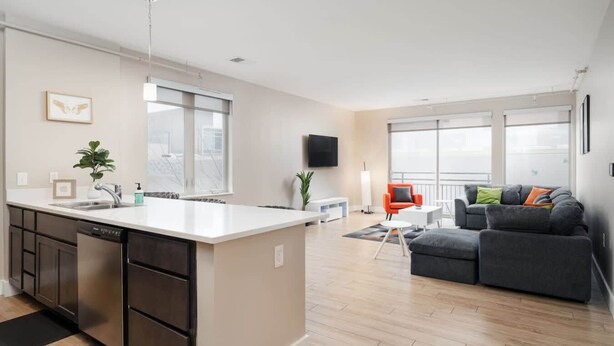 A modern apartment with a kitchen, dining area, and living room. It features a large island with a sink, a dining table, and a sofa. - Downtown Indy Private Room (Indianapolis)