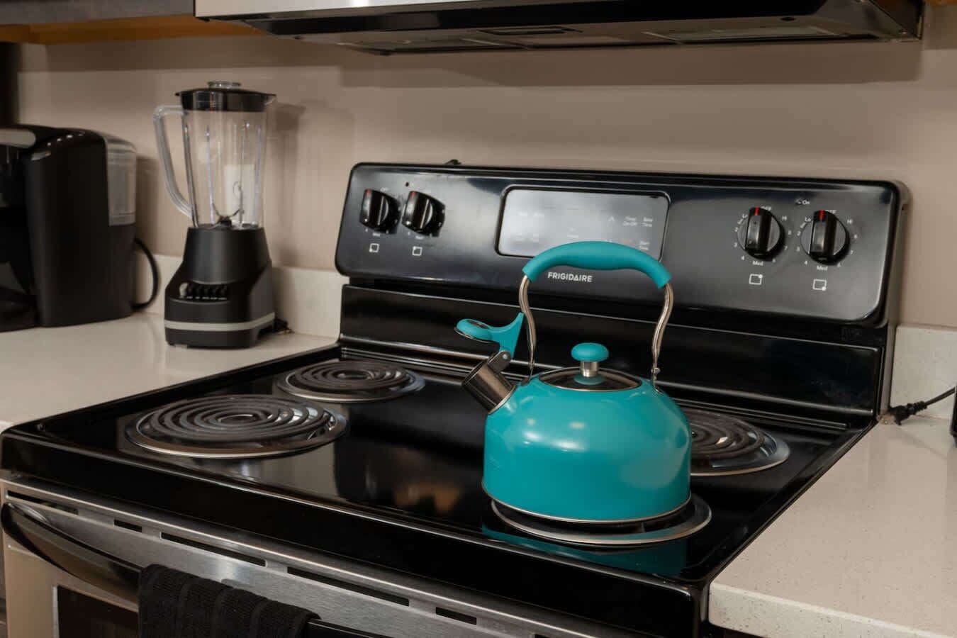 Una cocina con una estufa negra, una licuadora y un hervidor azul aguamarina.
