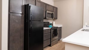 A modern kitchen with dark cabinetry, a black refrigerator, a microwave, a stove, and a sink. - Downtown Indy Private Room (Indianapolis)