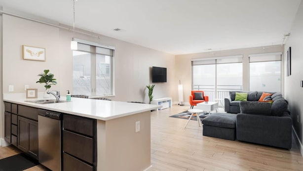 A modern apartment with a kitchen, dining area, and living room. It features a large island with a sink, a dining table, and a sofa. - Downtown Indy Private Room (Indianapolis)