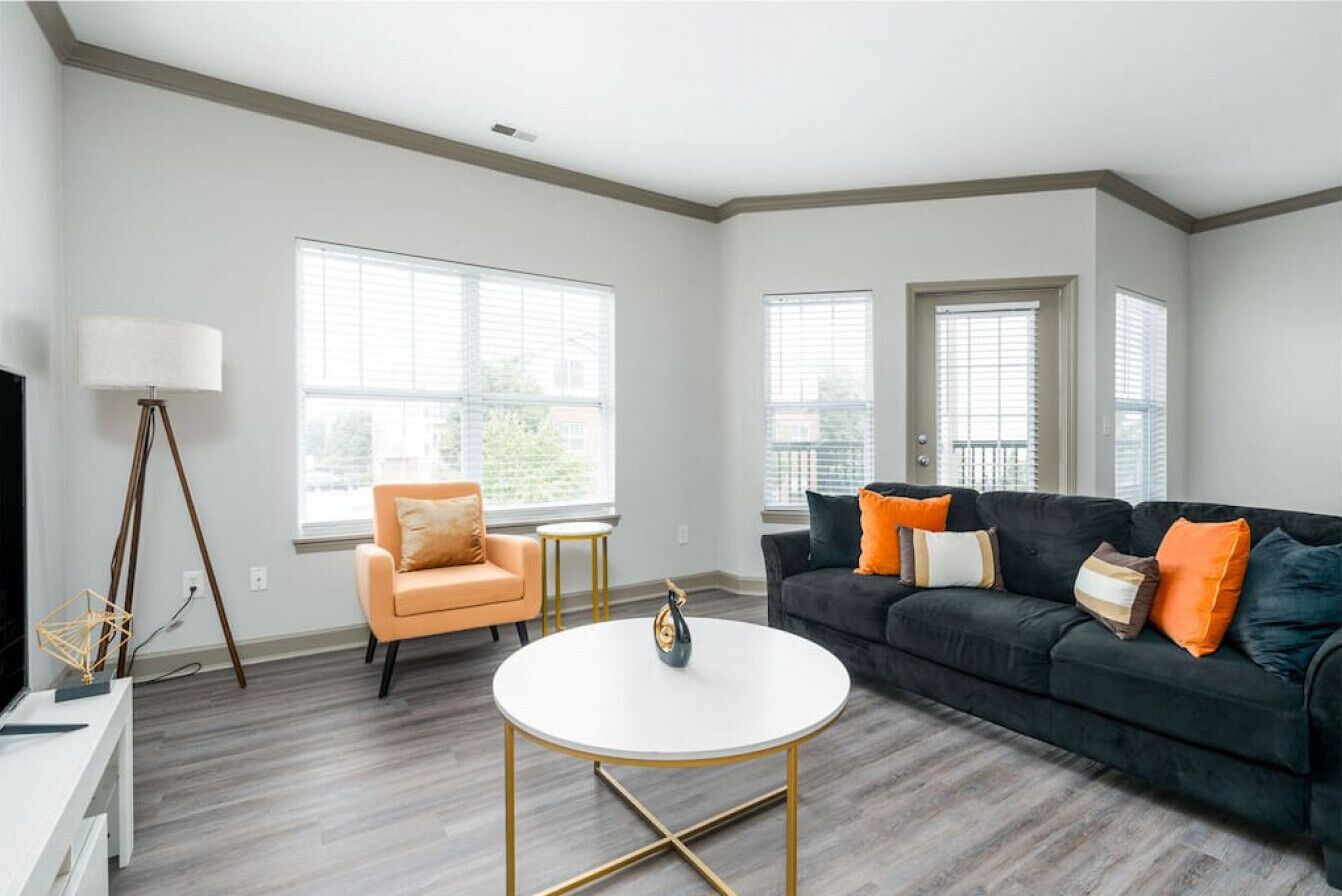 A living room with a black sofa, orange armchair, white coffee table, and a floor lamp.