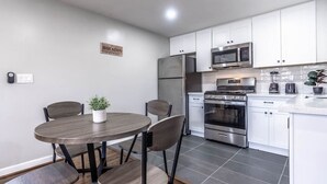 A modern kitchen with white cabinets, stainless steel appliances, and a dining area with a round table and chairs. - Spacious Apt Home 6 Min From Medical Center! (Houston)