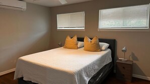 A bedroom with a bed, two windows with blinds, a ceiling fan, an air conditioner, and a bedside table with a lamp. - Spacious Apt Home 6 Min From Medical Center! (Houston)