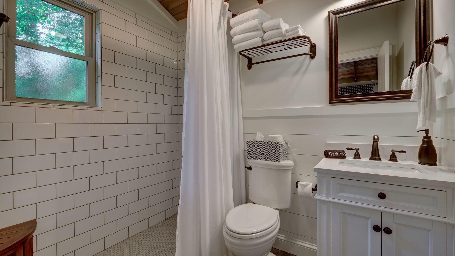 Ein Badezimmer mit weißen Fliesen, einer Toilette, einem Waschbecken mit Spiegel und einer Duschvorhang.