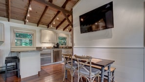 Une cuisine moderne avec des poutres en bois, un coin repas avec une table et des chaises en bois, et un grand téléviseur à écran plat fixé au mur.