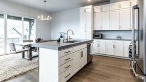 A modern kitchen with white cabinetry, a central island, stainless steel appliances, and a dining area with a bench and rug. - Modern Mountain Retreat Sleeps 10 Park City (Heber City)