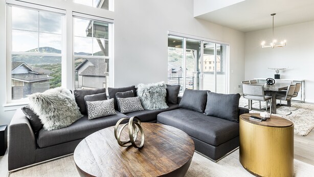 A modern living room with a sectional sofa, a round coffee table, and large windows offering a view of the surrounding landscape. - Modern Mountain Retreat Sleeps 10 Park City (Heber City)