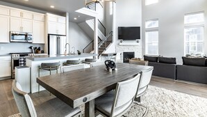 A modern kitchen with white cabinetry, a central island, and a dining area with a wooden table and chairs. - Modern Mountain Retreat Sleeps 10 Park City (Heber City)