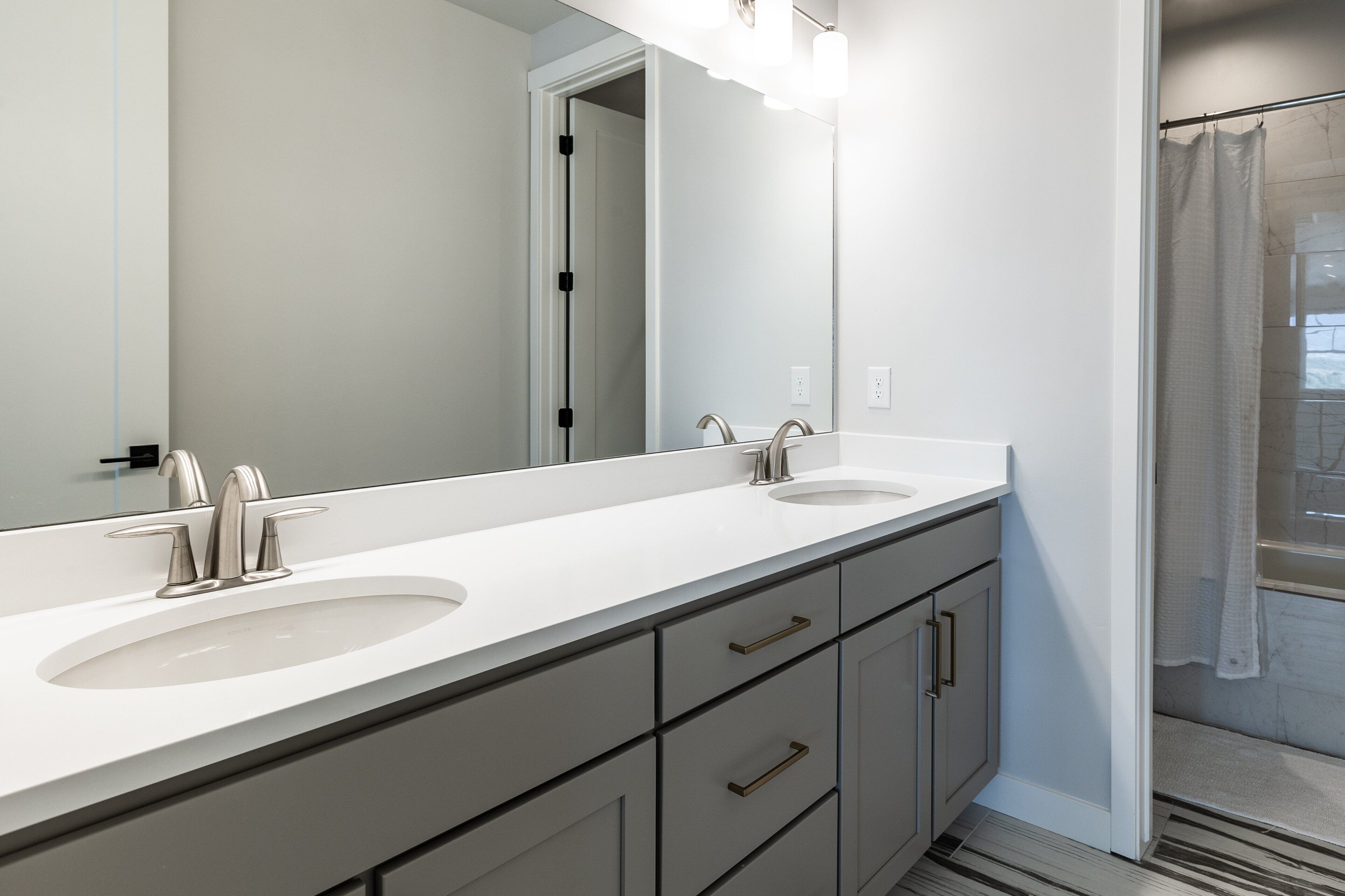 A modern bathroom with two sinks, a large mirror, and a shower area.
