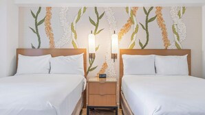 Habitación de hotel con dos camas, una mesita de noche con un reloj y una pared con motivos florales y de hojas.