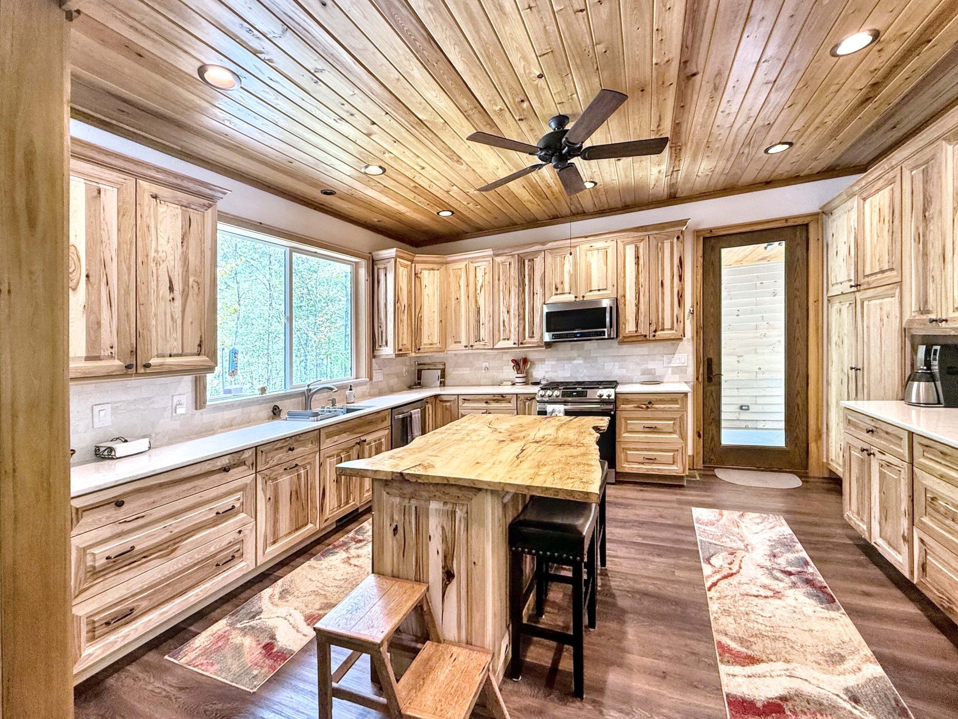A kitchen with wooden cabinets, a central island, a ceiling fan, and a view of the outdoors.