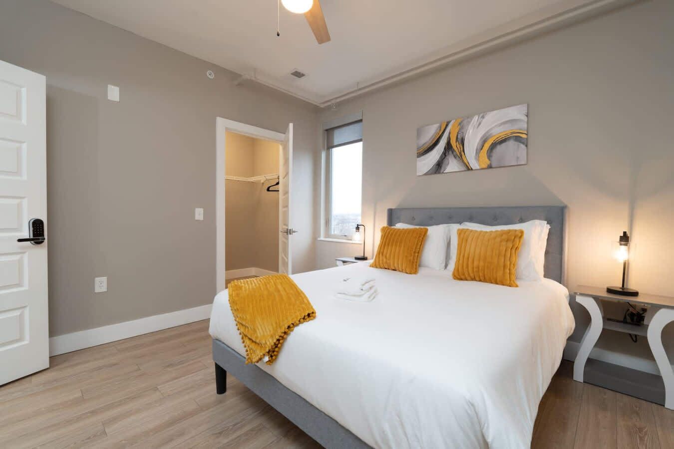 A modern bedroom with a large bed, a walk-in closet, and a view of the city.