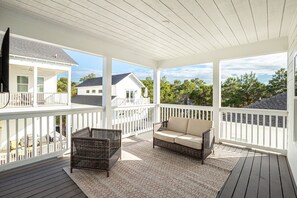 Eine überdachte Veranda mit Korbstuhl und Sofa, einem gemusterten Teppich und Blick auf benachbarte Häuser.