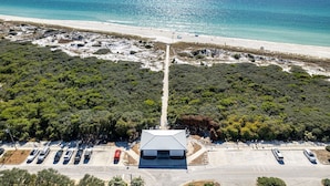Luftaufnahme einer Küstenlandschaft mit einem Parkplatz, einer Straße, die zum Strand führt, und dichter Vegetation.