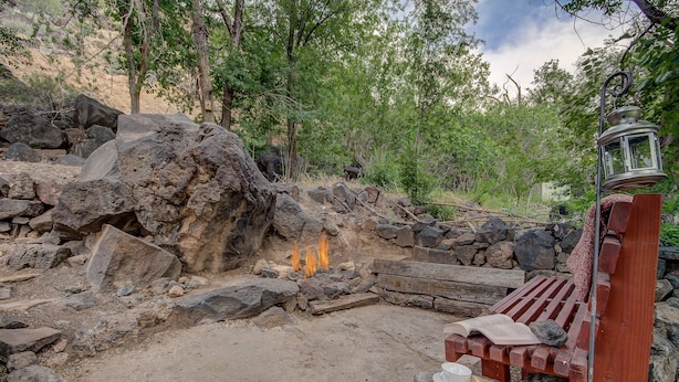 A rustic outdoor seating area with a stone fire pit, wooden benches, and a lantern.