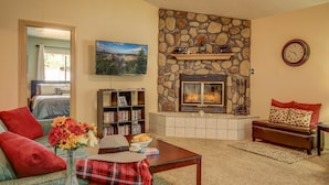 A cozy living room with a stone fireplace, a comfortable sofa, a coffee table with flowers, and a bookshelf.