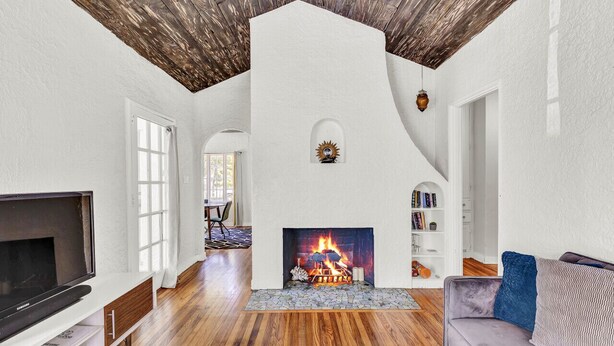 A living room with a fireplace, wooden flooring, a television, and a sofa. - Spanish Beach Bungalow Mainhouse (Holly Hill)