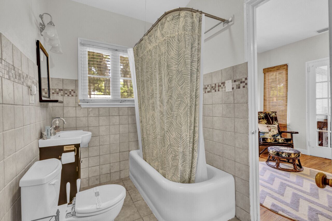A bathroom with a bathtub, toilet, sink, and a window with blinds.
