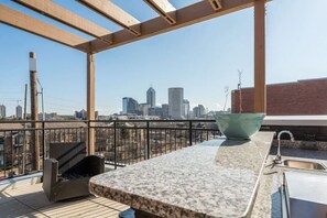 Una terraza en la azotea con una zona de cocina, un tazón verde grande y vistas al horizonte de la ciudad.