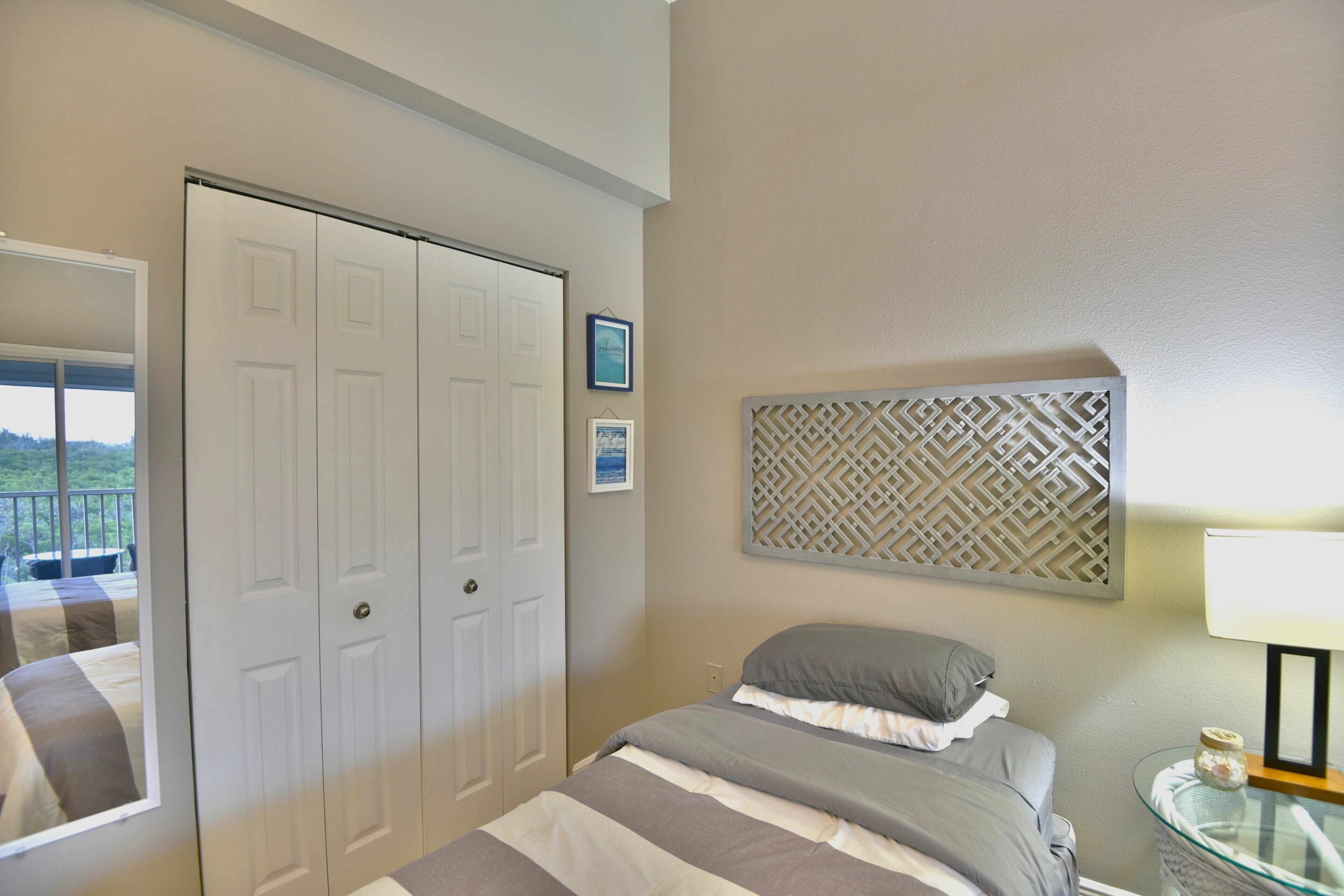 Une chambre à coucher comprenant un lit, une armoire, un panneau décoratif mural et une petite table avec une lampe.