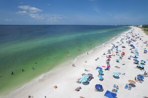 A beach with clear turquoise waters, numerous umbrellas, and people sunbathing. - Island Oasis (Holmes Beach)