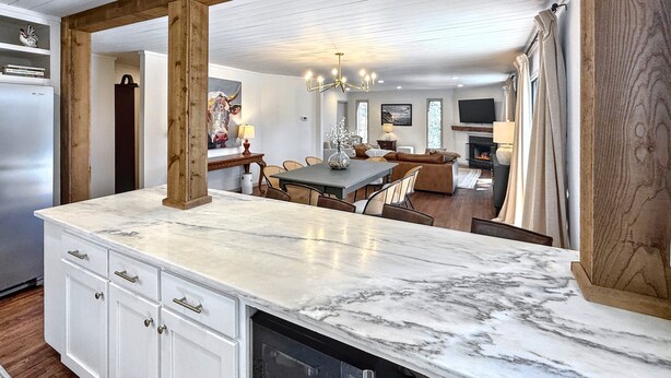 Una cocina con encimera de mármol, vigas de madera y vista al salón.