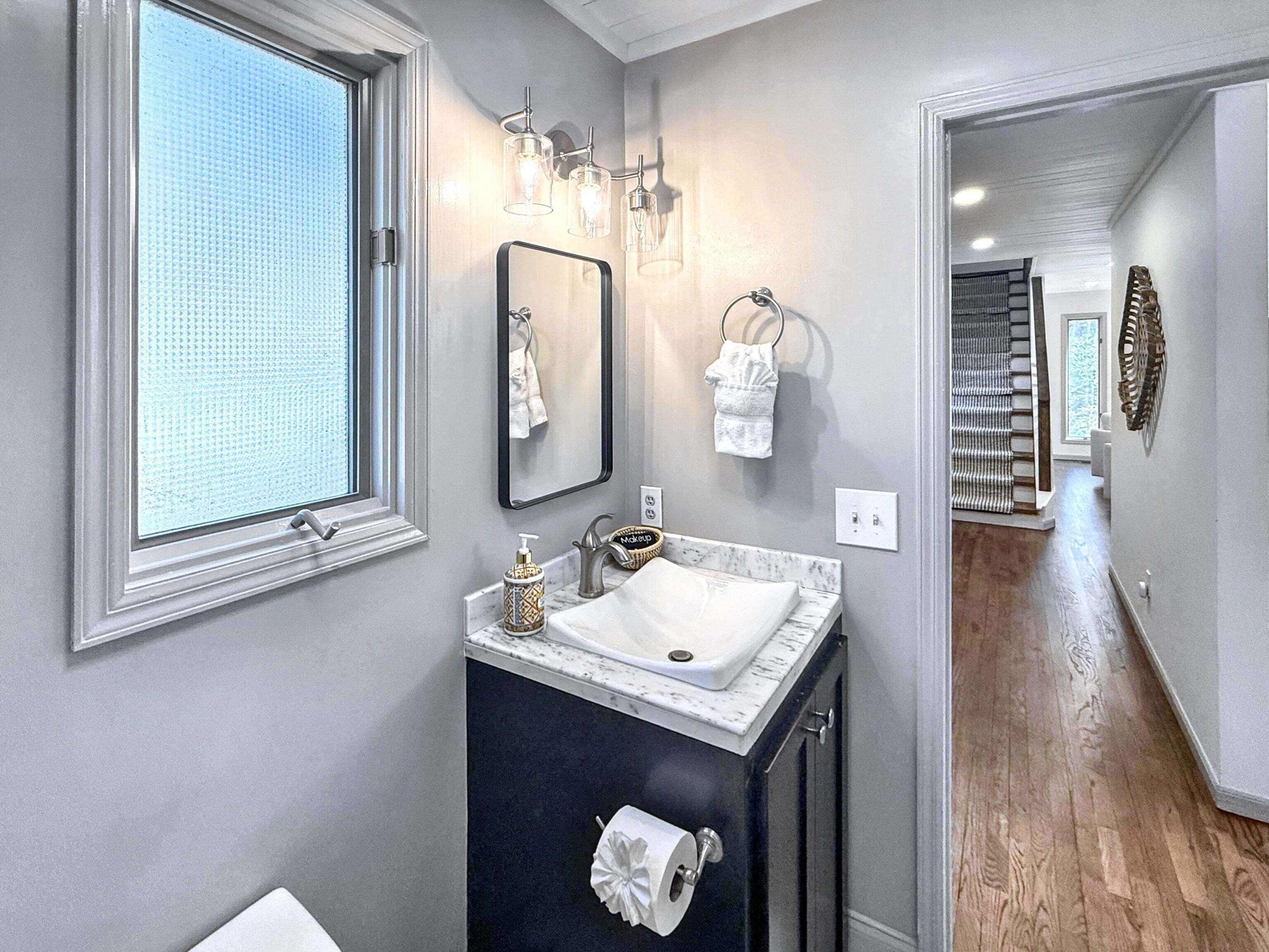 Une salle de bain dotée d’une grande fenêtre, d’un lavabo avec un plan de travail en marbre, d’un miroir et d’un porte-serviettes.