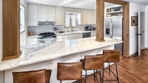 Una cocina moderna con armarios blancos, encimera de mármol, refrigerador de acero inoxidable y estructura con vigas de madera.