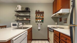 Une cuisine avec des plans de travail blancs, des armoires en bois, un four à micro-ondes, un évier, une cuisinière et un réfrigérateur.