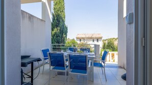 Un patio techado al aire libre con una mesa y sillas, una mesita con una botella, y una vista de un edificio al fondo.