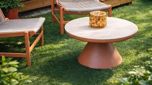 A modern outdoor seating area with a round table and two cushioned chairs, a wooden deck, and a glass door leading to a garden.