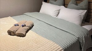 A neatly made bed with checkered bedding, two rolled towels, and a headboard with horizontal lines.