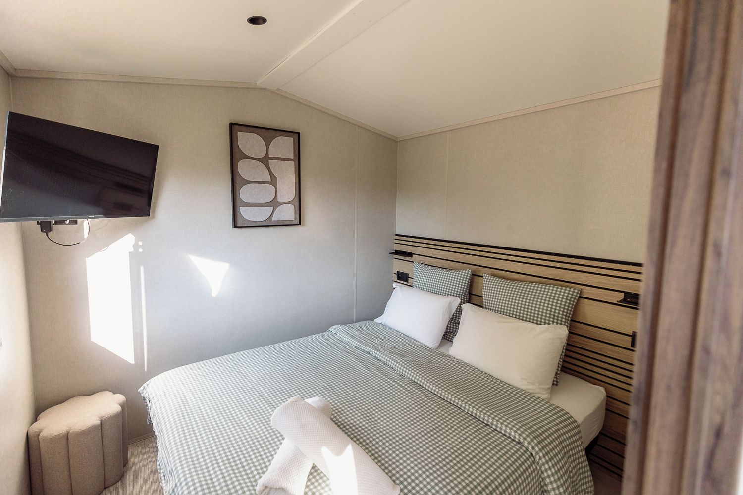 A bedroom with a bed, a television mounted on the wall, and a window providing natural light.